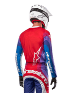 Motorcrosser van achteren gezien in Alpinestars 2024 Techstar Pneuma Jersey in Blue Mars Red White, met een rode rug met wit sterlogo, blauwe en paarse mouwen met witte branding, gecombineerd met bijpassende broek en een witte helm voor off-road racing.
