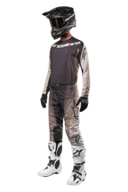 Motorcrosser in volledige race-uitrusting, 2024 Techstar Pneuma Jersey in Dark Sand en Iron Dust Gray, bijpassende crossbroek met patroon, zwarte helm met goggle, wit-zwarte laarzen en zwarte handschoenen, gecoördineerde outfit voor off-road racen