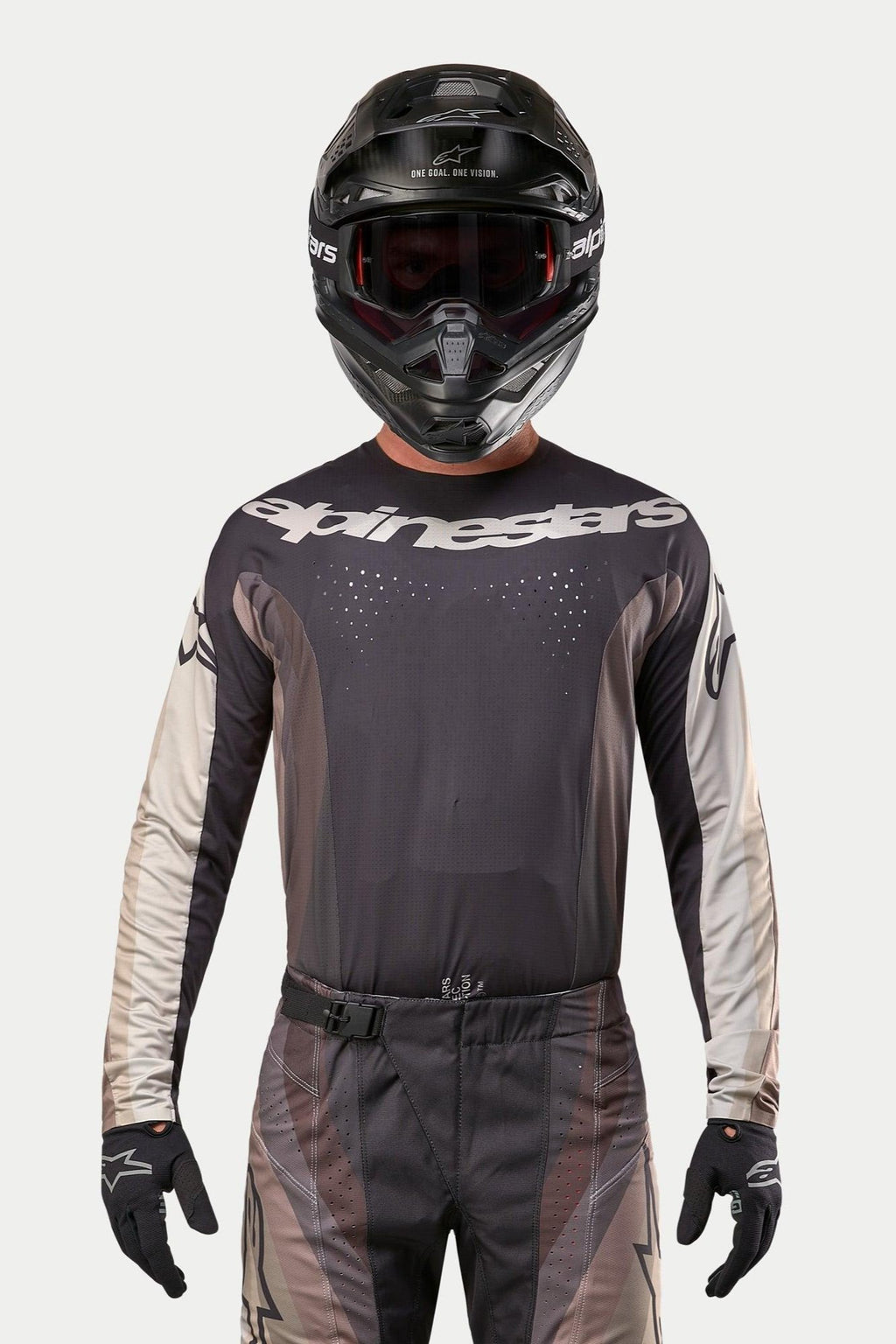 Alpinestars 2024 Techstar Pneuma Jersey, motorcross jersey, Dark Sand en Iron Dust Gray, gedragen met bijpassende crossbroek en zwarte helm, voorzien van een prominent Alpinestars-logo op de borst en lasergesneden ventilatieperforaties, performance off-road racekleding.