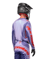 Alpinestars 2024 Techstar Ocuri Jersey, motocross jersey, paars en feloranje, achteraanzicht van een rijder in bijpassende kleding met een zwarte helm, voorzien van grote oranje Alpinestars-belettering op de mouwen en onderrug