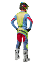 Motorcrosser van achteren gezien in de Alpinestars 2024 Techstar Ocuri Jersey, lichtblauw met geel fluo en Red Berry accenten, bijpassende racebroek, witte laarzen en neon helm, complete off-road uitrusting voor professionele competitie