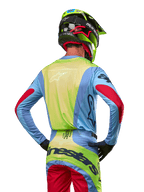 Motocrosser van achteren in de Alpinestars 2024 Techstar Ocuri Jersey, lichtblauw met fluogeel op de rug en rode accenten op de mouwen, bijpassende crossbroek en neongele helm, gecoördineerde outfit voor off-road racing