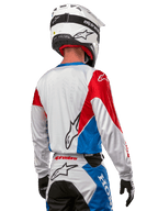 Motorcrosser in het Alpinestars Honda Racer Iconic Jersey, achteraanzicht, wit met felblauwe en felrode panelen, opvallend Alpinestars-logo op de rug, gecombineerd met een witte motorcrosshelm en bijpassende crossbroek