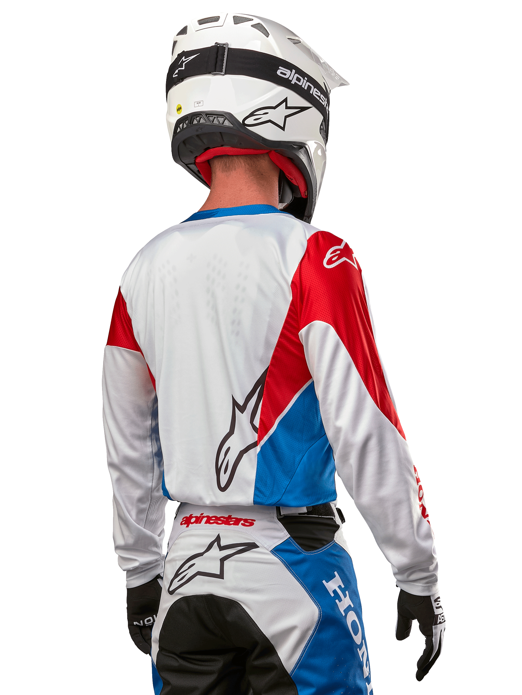 Motorcrosser in het Alpinestars Honda Racer Iconic Jersey, achteraanzicht, wit met felblauwe en felrode panelen, opvallend Alpinestars-logo op de rug, gecombineerd met een witte motorcrosshelm en bijpassende crossbroek
