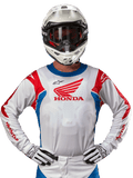 Alpinestars Honda Racer Iconic Jersey, wit motorcross shirt met een rood Honda-logo en felblauwe en rode accenten, gedragen door een rijder met een witte helm en handschoenen, prestatiegerichte kleding voor off-road en motorcross