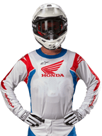 Alpinestars Honda Racer Iconic Jersey, wit motorcross shirt met een rood Honda-logo en felblauwe en rode accenten, gedragen door een rijder met een witte helm en handschoenen, prestatiegerichte kleding voor off-road en motorcross