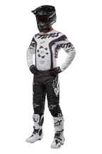 Motorcrosser in volledige uitrusting met het Alpinestars 2024 Racer Hana Jersey in wit en zwart, zwarte crossbroek met witte logo's, zwarte helm, wit-zwarte crosslaarzen en zwarte handschoenen, professionele off-road race-outfit
