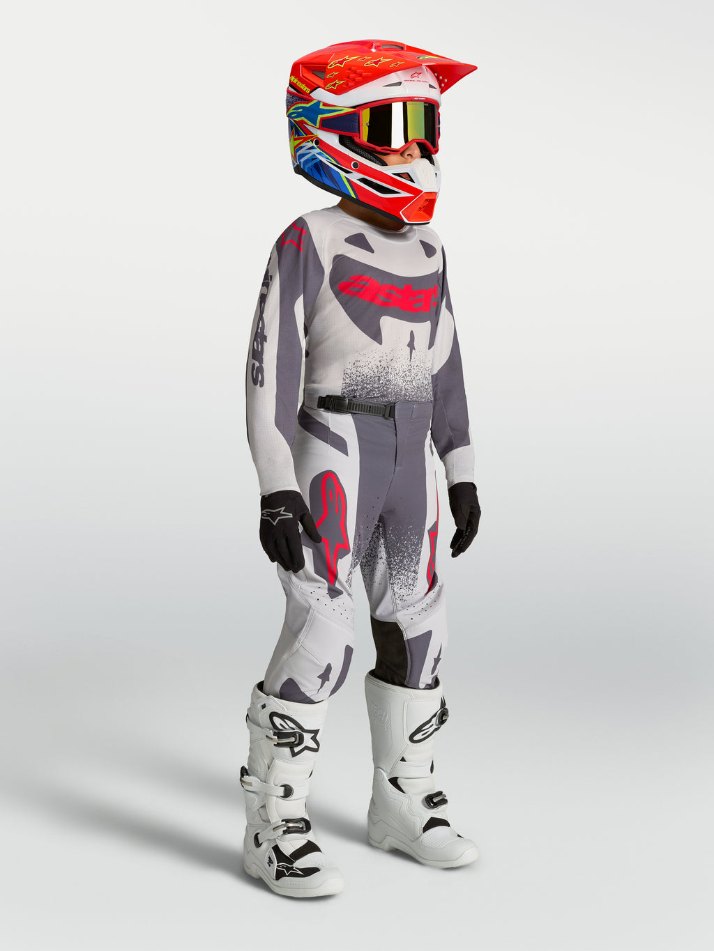 Alpinestars Jeugd Supertech Swan jersey en gear set, grijs en rood fluo motocross-outfit met witte motorlaarzen.