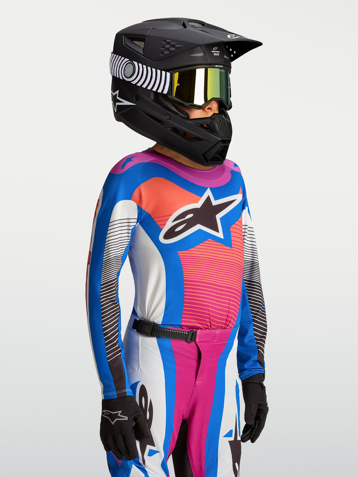 Alpinestars Jeugd Supertech Maven Jersey, ademende motocrossjersey, blauw en koraal, gedragen met een zwarte helm.