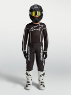 Alpinestars jeugd Fluid Apex V2 jersey en gear set, zwart-zilveren motocross-outfit met witte motorlaarzen en helm.