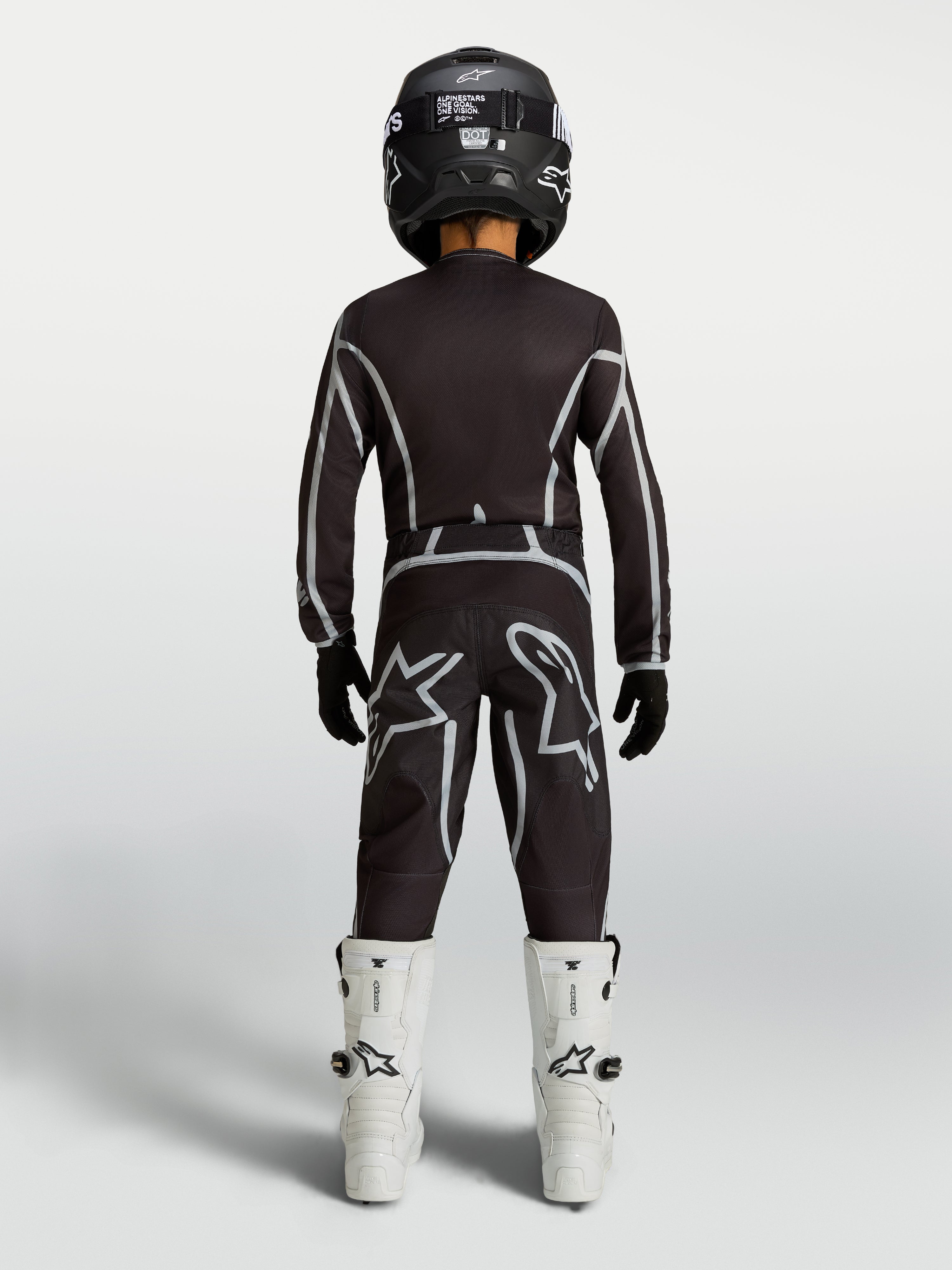Alpinestars Jeugd Fluid Apex V2 jersey en motocrossuitrusting, zwart en zilver, achteraanzicht met witte motorlaarzen.