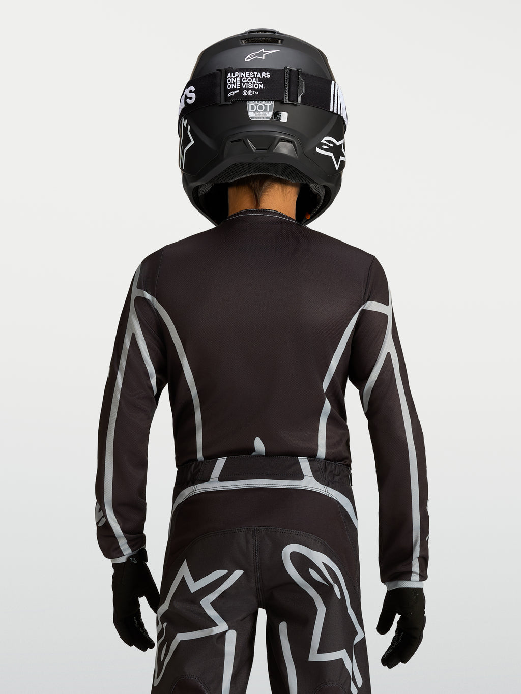 Alpinestars jeugd Fluid Apex V2 jersey, zwart en zilver, motocrossjersey met ergonomische pasvorm, achteraanzicht van jonge rijder in off-road uitrusting.