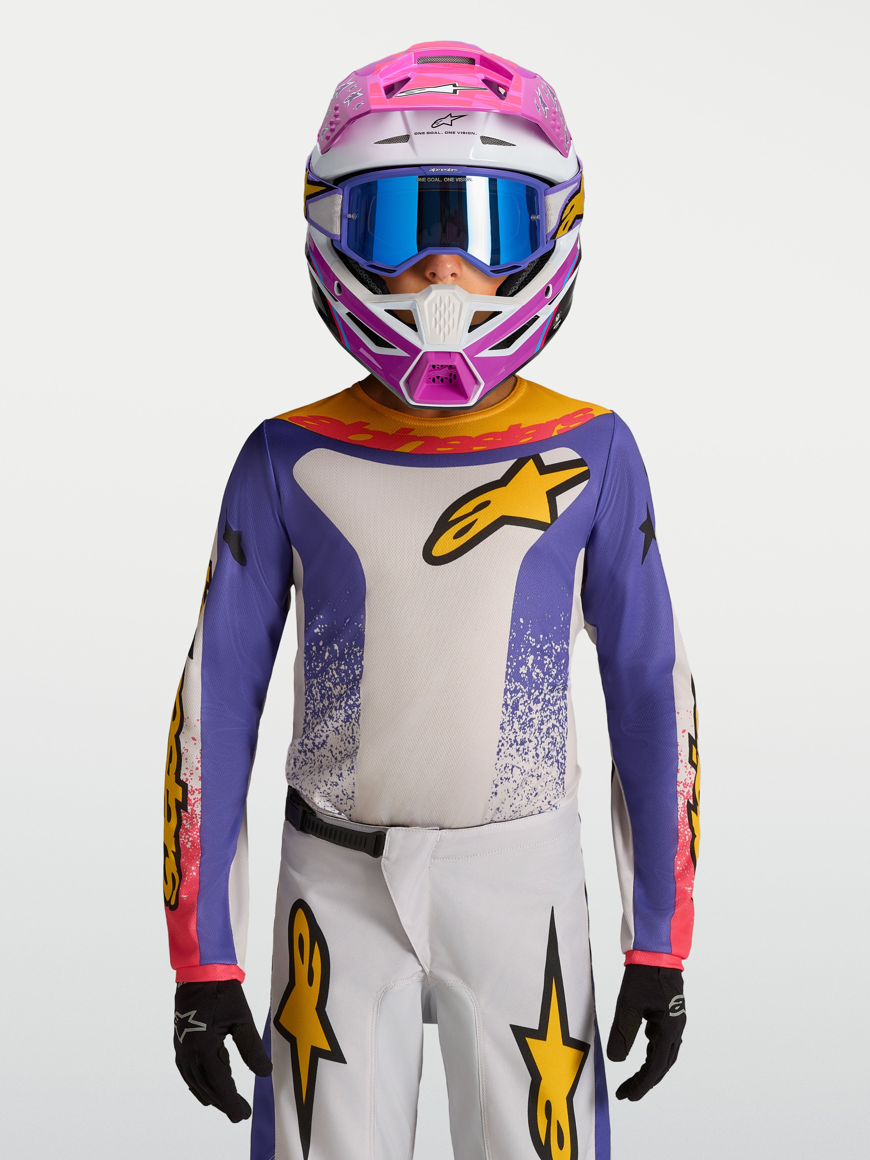 Alpinestars Jeugd Fluid Drag Jersey 2027, motocrossjersey voor kinderen in blauw en wit met goudkleurige accenten, ademend polyfabric voor off-road rijden, gedragen door een model met helm en handschoenen.