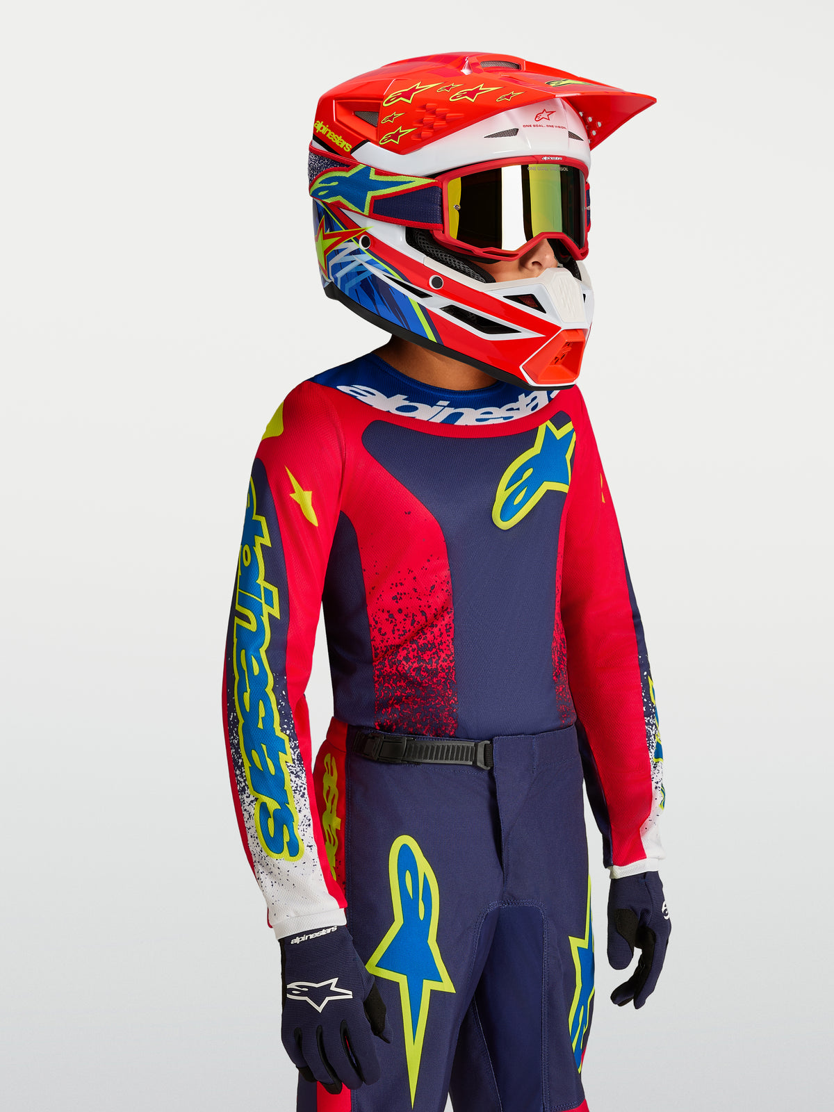 Alpinestars Jeugd Fluid Drag Jersey in blauw en rood, motorcrossuitrusting voor kinderen met bijpassende helm.