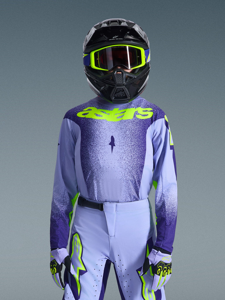 Youth motocross rider wearing the 2026 Youth Supertech Scenz Jersey, Purple and Yellow Fluo colorway, featuring a lavender and dark purple gradient with bright yellow Astars logo, paired with matching pants, gloves, and a black helmet with yellow goggles for off-road racing.