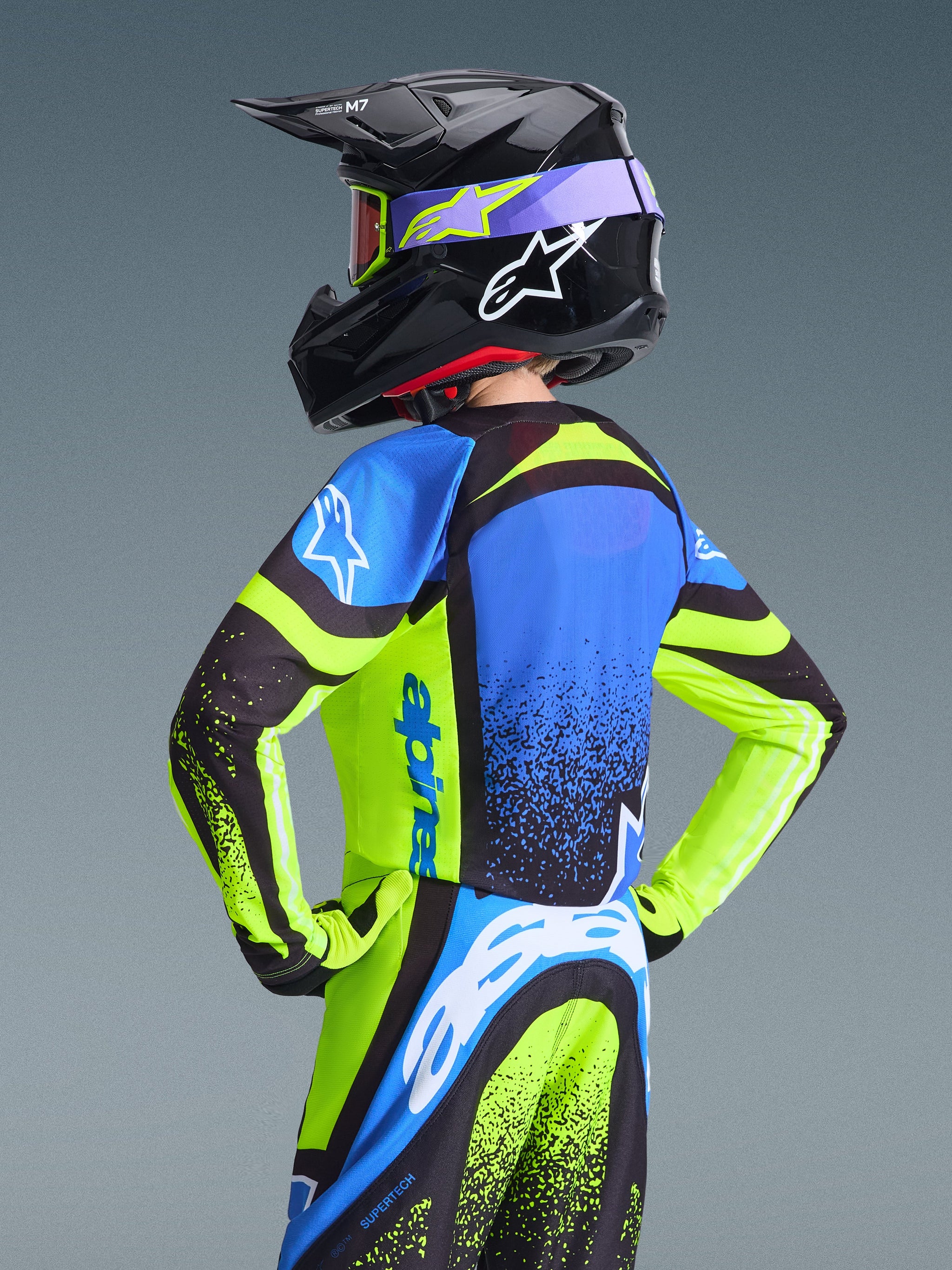 Jeugd motocrossrijder van achteren in de Alpinestars 2026 Youth Supertech Nomur Jersey, Dark Navy en Yellow Fluo met blauwe accenten, gecombineerd met een bijpassende zwarte helm en broek, professionele off-road race-uitrusting.