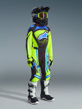 Jeugd motocrossrijder in complete race-uitrusting, 2026 Youth Supertech Nomur Jersey in Yellow Fluo en Dark Navy, bijpassende broek met blauwe accenten, zwarte helm met fluogele crossbril, witte en zwarte laarzen, gecoördineerde outfit voor off-road racen.