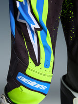 Alpinestars 2026 Youth Supertech Nomur motocross-uitrusting, close-up van een motorcrossbroek in Dark Navy en Yellow Fluo met UCLA Blue accenten, voorzien van het astars-logo en lasergesneden ventilatieperforaties, technische racekleding