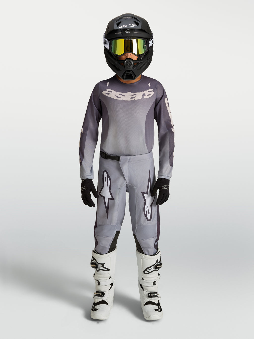 Alpinestars Jeugd Fluid Amber jersey en gear set, motorcrossuitrusting, grijs en zand, zwarte helm en witte motorlaarzen.
