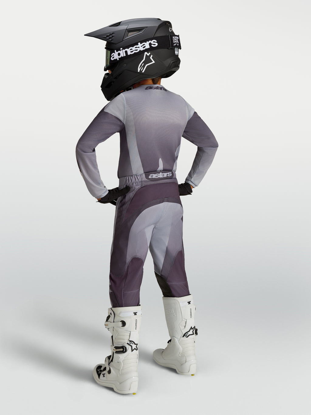 Alpinestars Jeugd Fluid Amber gear set, grijs en paarse motocrossoutfit met helm en witte motorlaarzen, achteraanzicht.