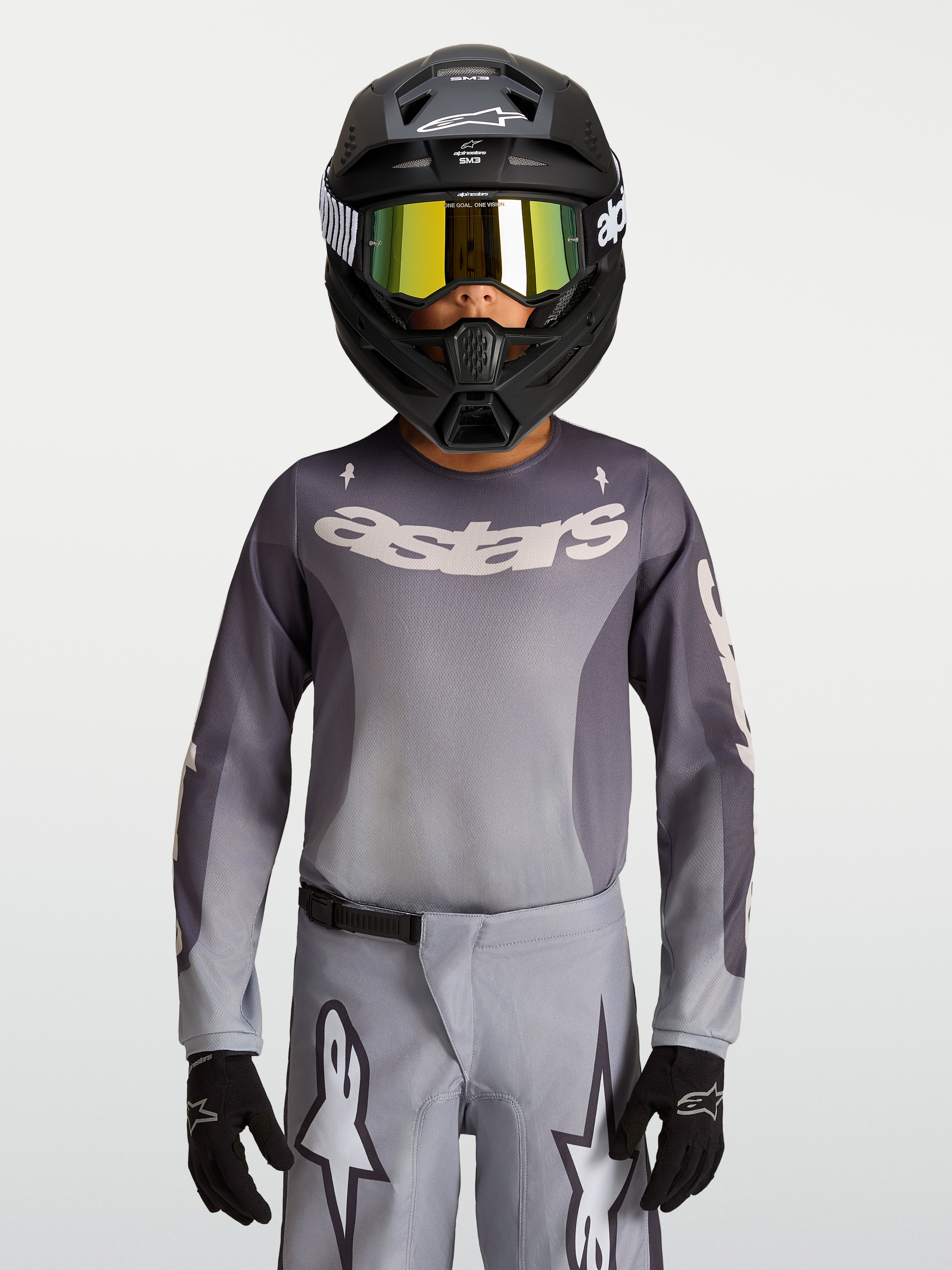 Alpinestars Jeugd Fluid Amber jersey, ademend motorcrossjersey in grijs en zand, gedragen door een jonge rijder met helm.