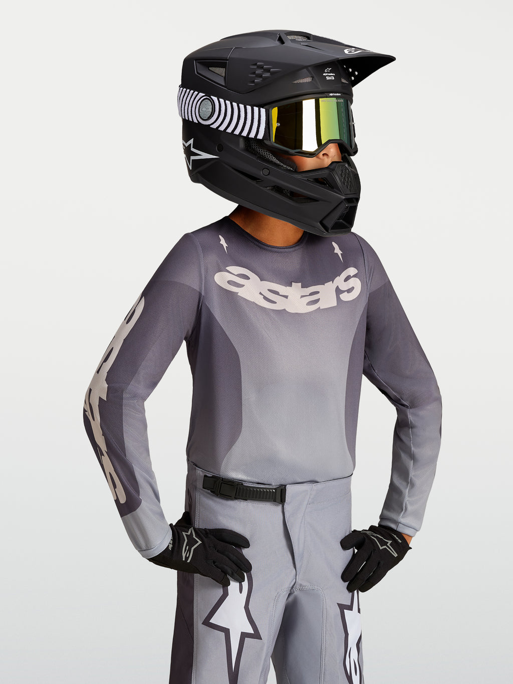 Alpinestars Jeugd Fluid Amber Jersey 2027, motocrossjersey in zand en grijs, gedragen met een zwarte helm en crossbril.