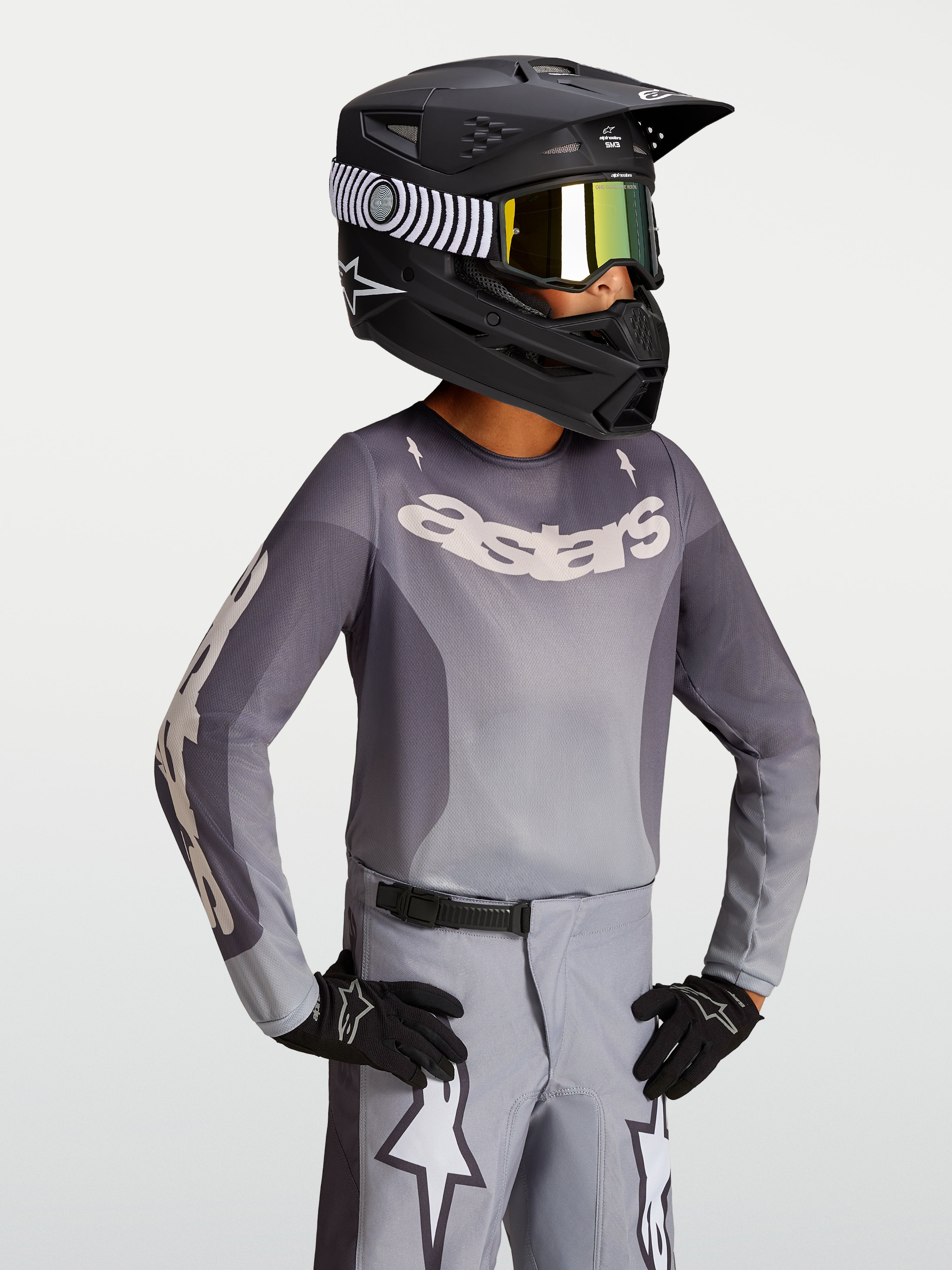 Alpinestars Jeugd Fluid Amber Jersey 2027, motocrossjersey in zand en grijs, gedragen met een zwarte helm en crossbril.