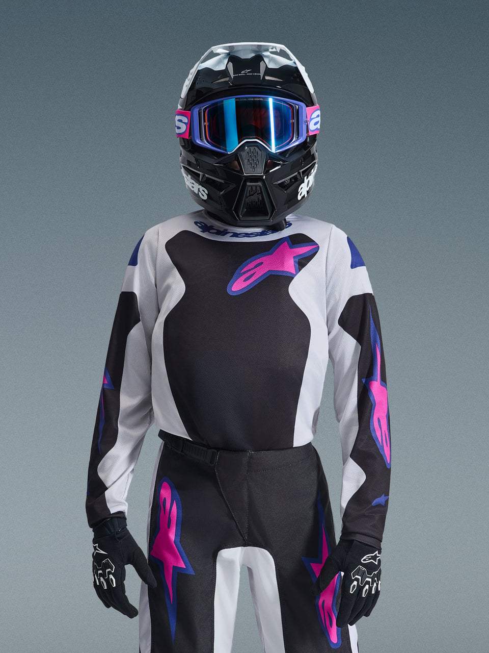 Young motocross rider wearing the Alpinestars 2026 Youth Fluid Grid Jersey in Black, Light Gray, and Purple, paired with matching grid-patterned pants, black helmet with blue-lensed goggles, and black gloves, complete gear set for youth off-road racing.