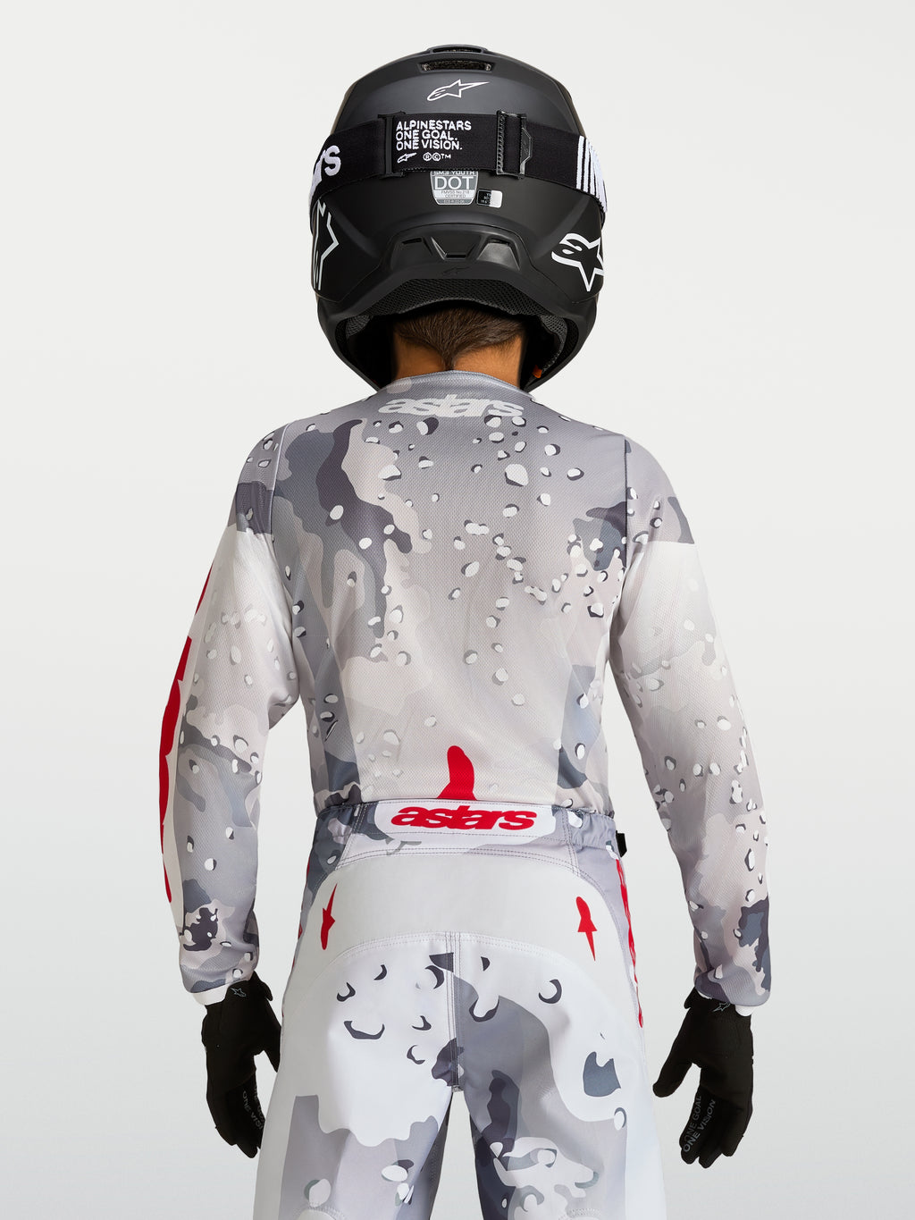 Alpinestars Jeugd Fluid Lone Jersey 2027, grijze camouflage motorcrossjersey, achteraanzicht met rode accenten en helm.