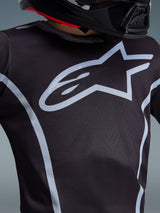 Alpinestars 2026 Youth Fluid Apex Jersey, detailopname van het borstontwerp, zwart en grijs, met een opvallend lichtgrijs sterlogo en sportieve biezen, gedragen met een zwarte helm, performance motorcrossuitrusting voor jonge rijders