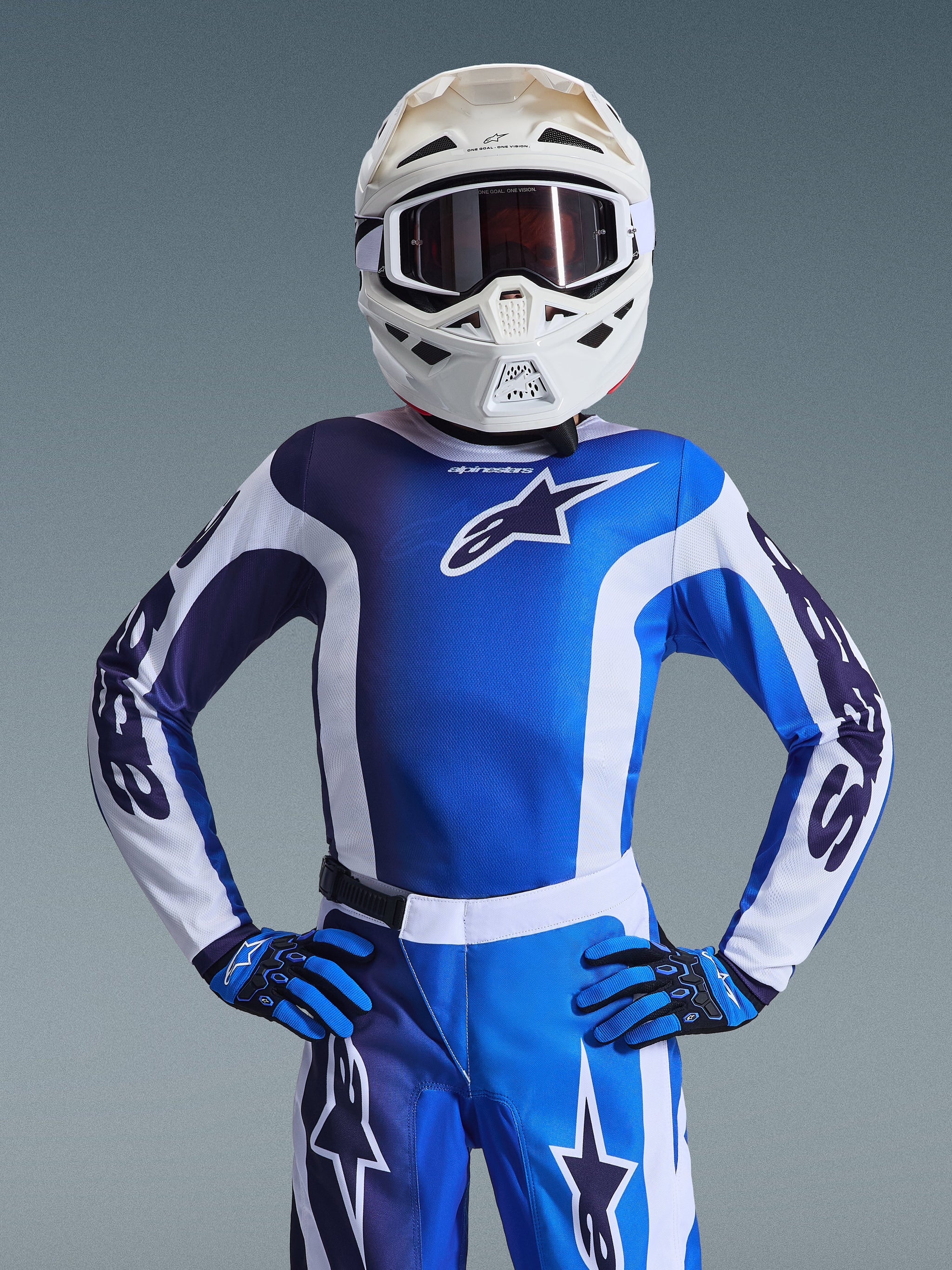 Jeugd motocrossrijder die de 2026 Youth Fluid Portl Jersey in Ucla Blue White draagt, met bijpassende blauwe en witte motorcrossbroek, blauwe en zwarte handschoenen en een witte helm met bril, complete race-uitrusting voor jonge off-road rijders.