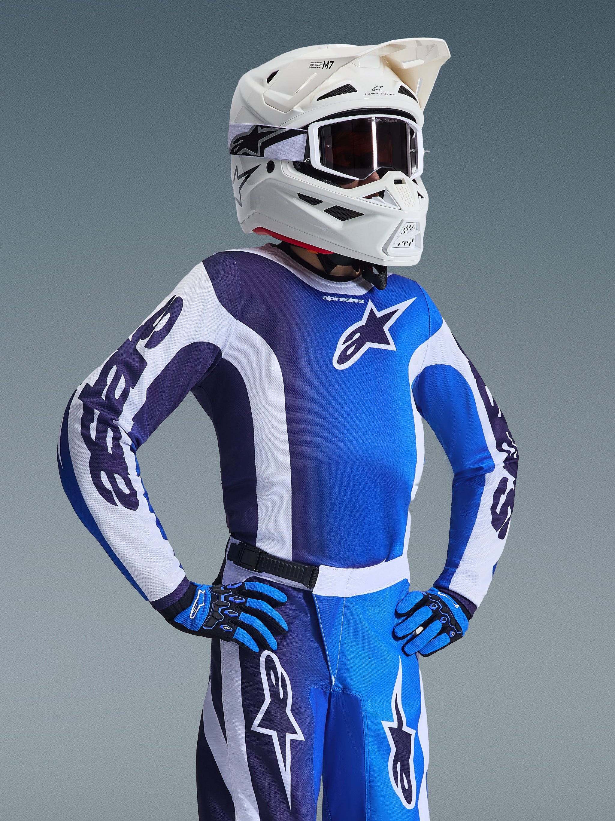 Alpinestars 2026 Youth Fluid Portl Jersey, jeugd motorcross shirt, UCLA blauw en wit, met een kleurgeblokt ontwerp en ster-logo, gedragen met bijpassende broek, handschoenen en een witte helm met bril, gecoördineerde race-uitrusting voor jongeren
