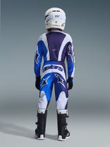 Jeugd motocrossrijder in complete race-uitrusting vanaf de achterkant gezien, Ucla Blue en White Fluid Portl Jersey, bijpassende broek met grote sterlogo's en 'astars' branding, witte helm en zwarte laarzen, gecoördineerde professionele outfit voor off-road rijden.