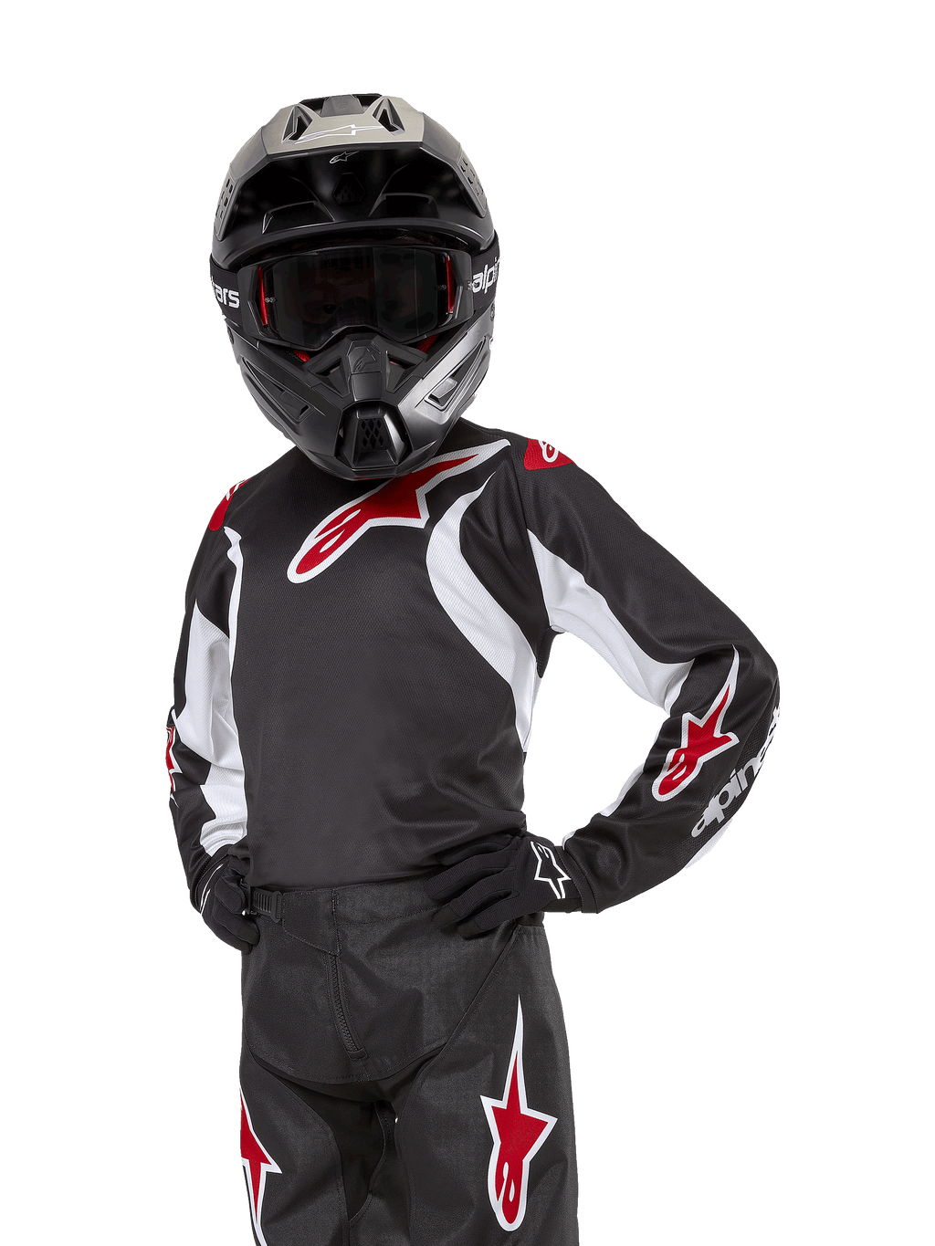 Alpinestars Youth 2024 Racer Lucent Jersey, motorcross jersey, zwart, wit en rood, gedragen door een jeugdrijder met een zwarte helm en bijpassende broek, voorzien van rode sterlogo's en witte grafische accenten, technische off-road kleding voor motorcross