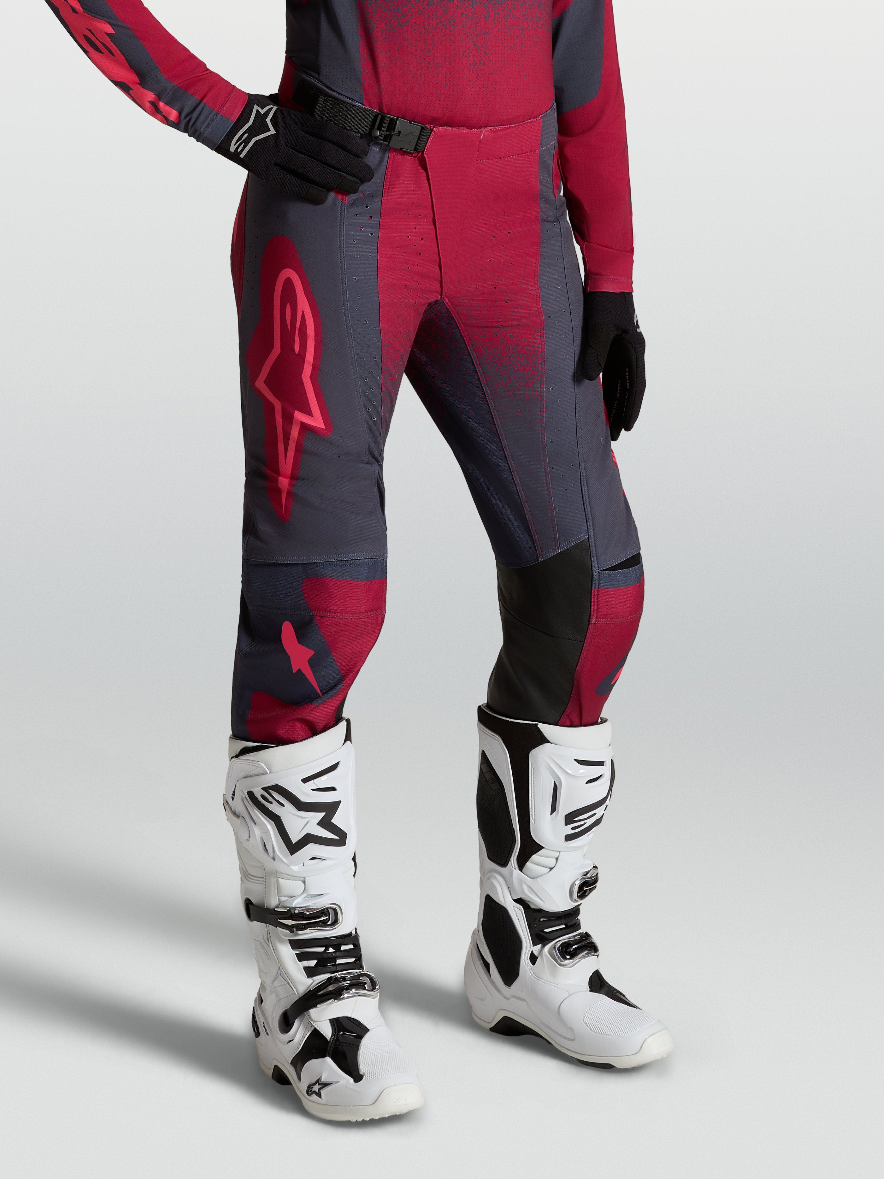 Alpinestars Stella Techstar Swan broek, dames-motocrossbroek, rood en donkergrijs, gedragen met witte Tech 10 motorlaarzen.