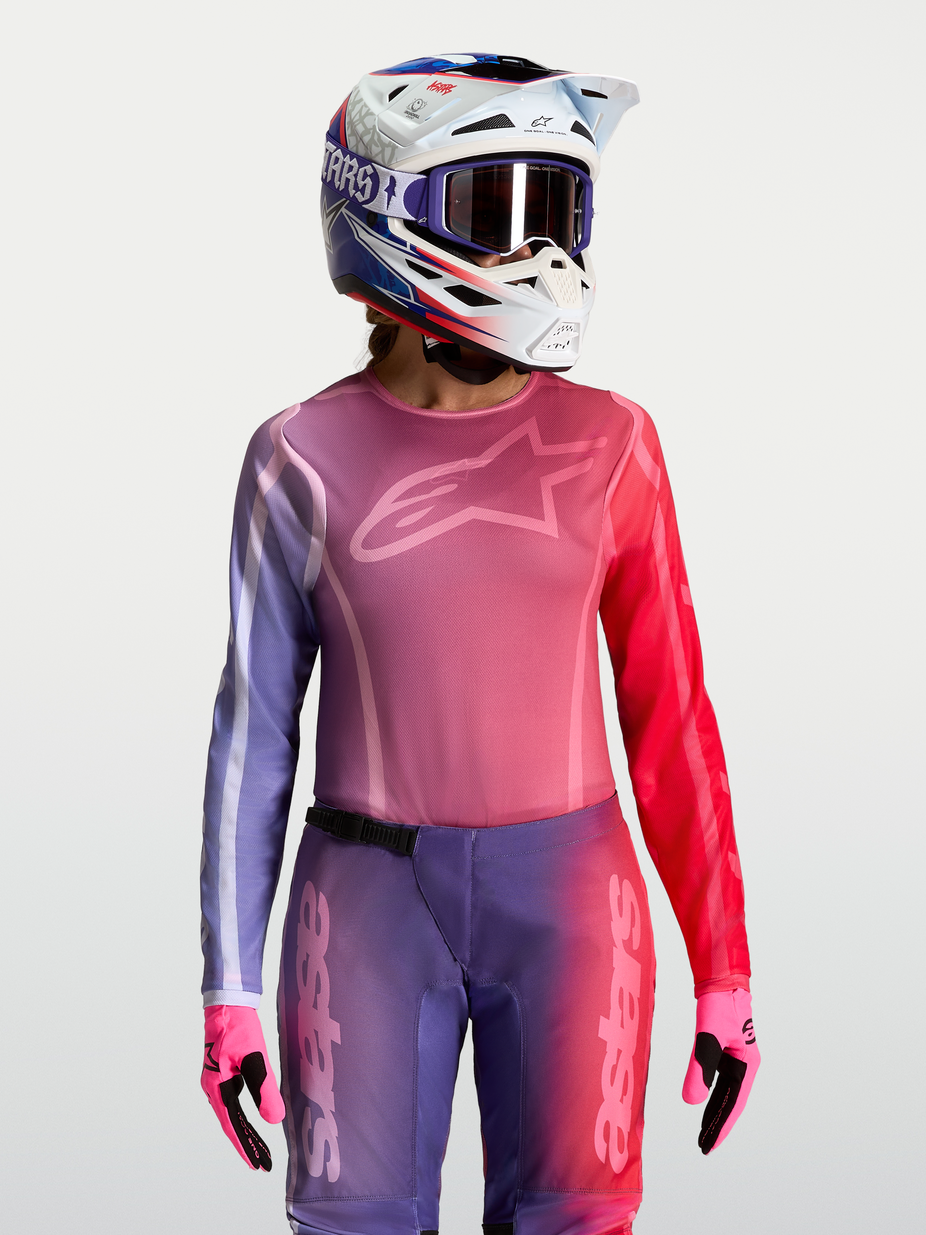Alpinestars Stella Fluid Kepler jersey, dames motocross-top in paars en rood, athletische pasvorm, vochtafvoerend polyfabric, gedragen met bijpassende helm en handschoenen.
