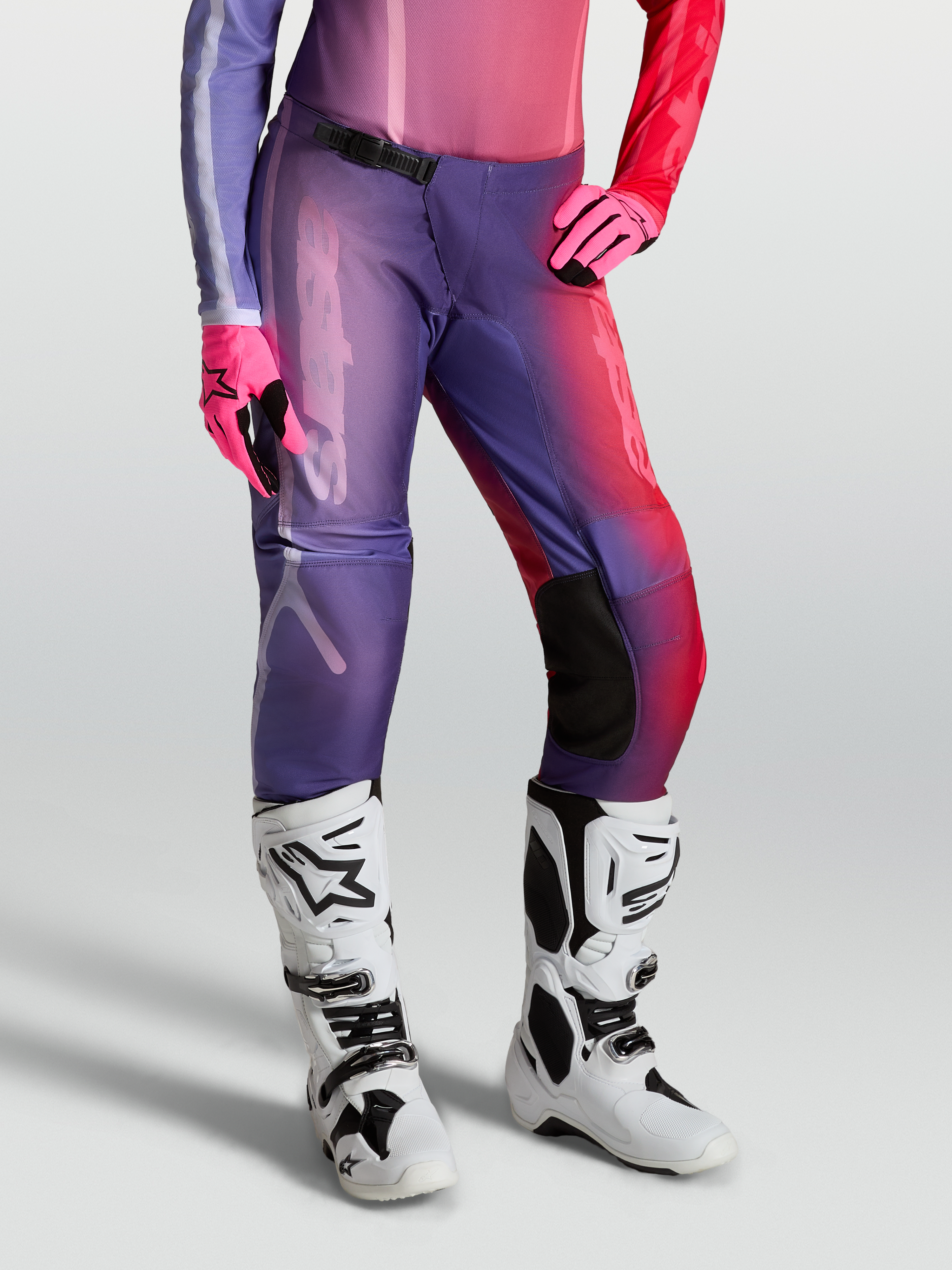 Alpinestars Stella Fluid Kepler Broek, motocrossbroek voor dames, paars en rood, gedragen met witte laarzen en roze handschoenen.