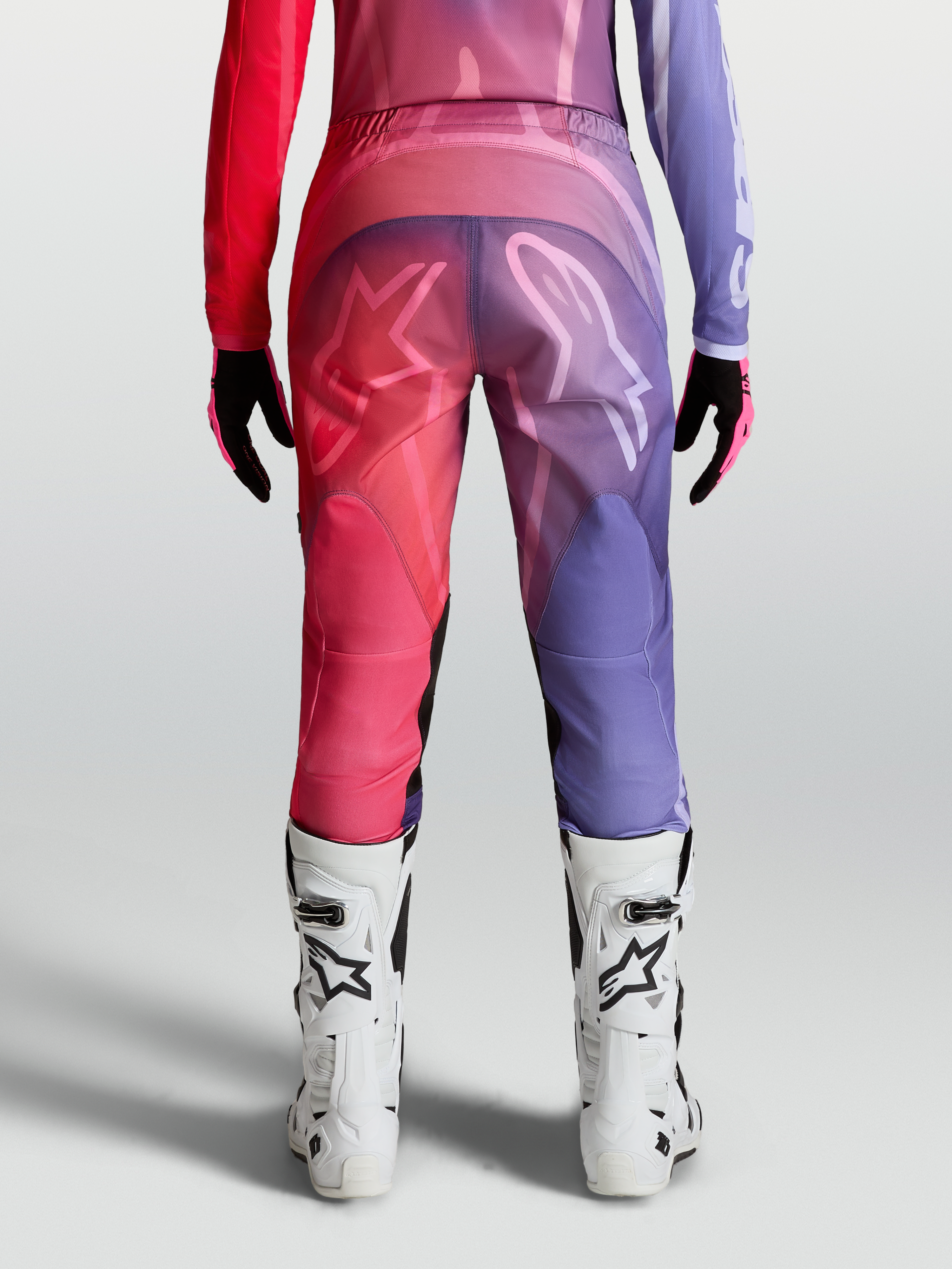 Alpinestars Stella Fluid Kepler Broek, paarse en roodroze dames motorcrossbroek met ergonomische pasvorm en witte MX-laarzen.
