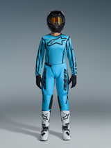 Motocross rider wearing the 2026 Alpinestars Stella Fluid Apex Jersey and matching pants in light blue with black accents, black helmet with gold goggles, white and black boots, and black gloves, complete women's off-road gear set.