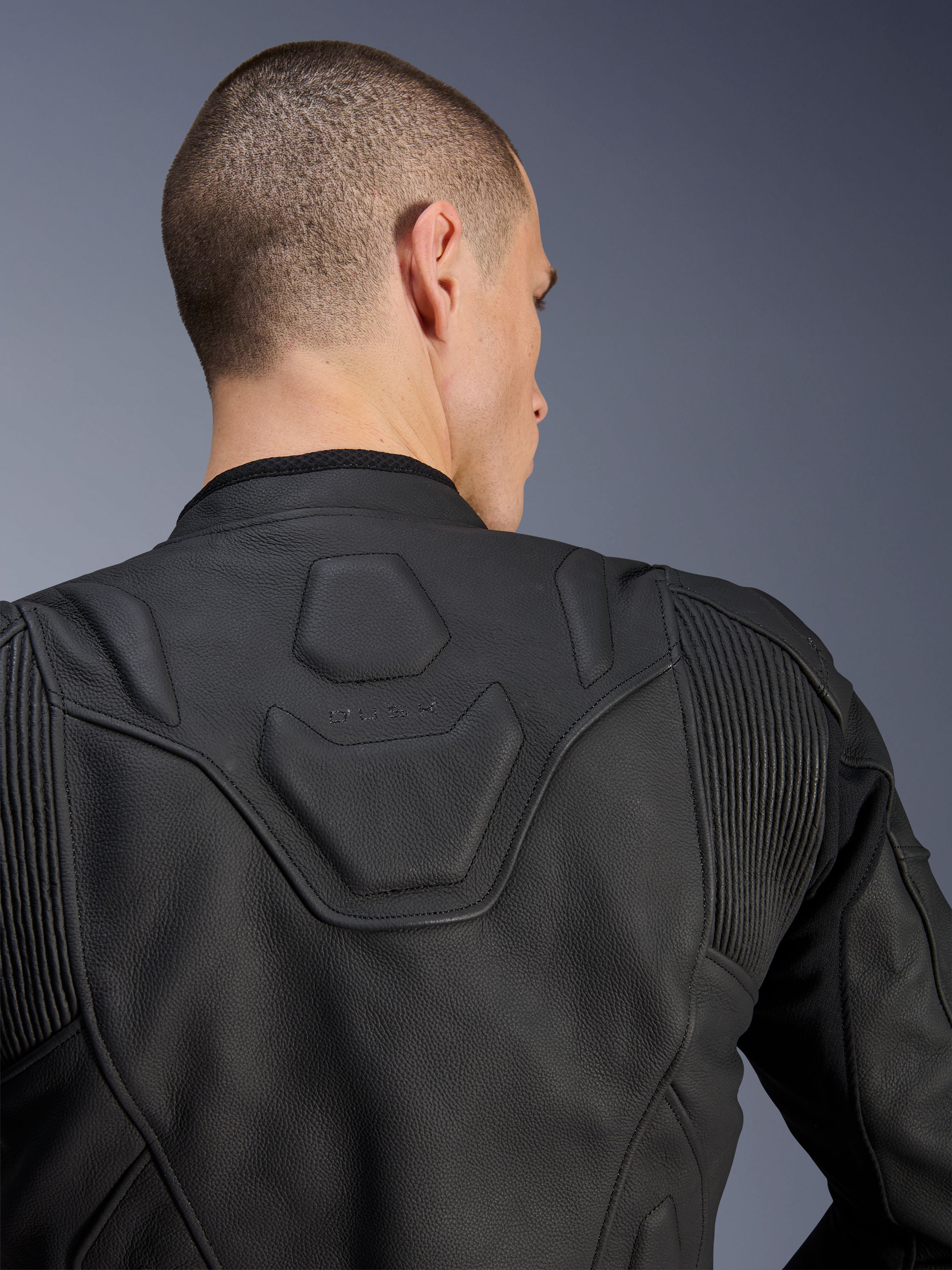 Alpinestars Dusk leren jas, zwart, close-up van de bovenrug en schouders met het DUSK-logo in reliëf op een gewatteerd paneel, lederen accordeon stretch-inzetstukken, premium runderleren constructie