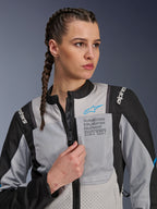 Vrouw die de Alpinestars Stella ST-2 Air Jacket in Ice Gray en Black draagt, close-up portret, met mesh-panelen voor ventilatie, 'ALPINESTARS EXPLORATION EQUIPMENT' branding op de borst met een blauw logo, moderne adventure motorjas