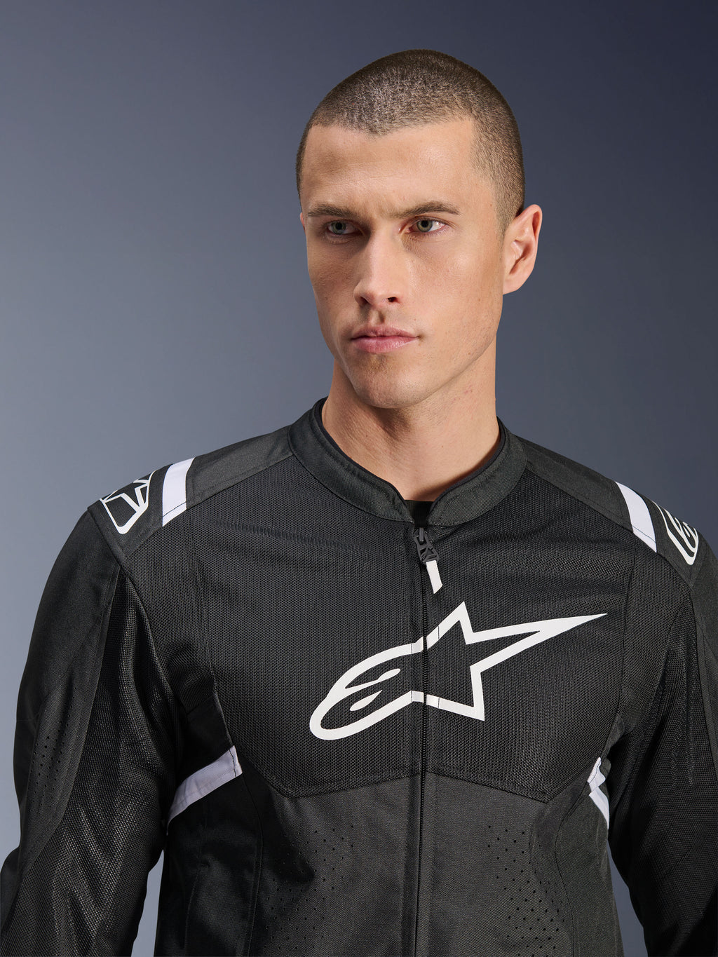 Alpinestars T-SPS Air V2 Jas, textiel motorjas, zwart en wit, voorzien van een groot wit logo op de borst en mesh-panelen, sportieve pasvorm gedragen door een mannelijk model