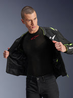 Mannelijk model dat de Alpinestars T-Sps Air V2 Jas in Black Yellow Fluo draagt, open getoond om de interne mesh-constructie en zakken te benadrukken, gecombineerd met een zwarte Alpinestars base layer en zwarte broek, stedelijke motorrijstijl.