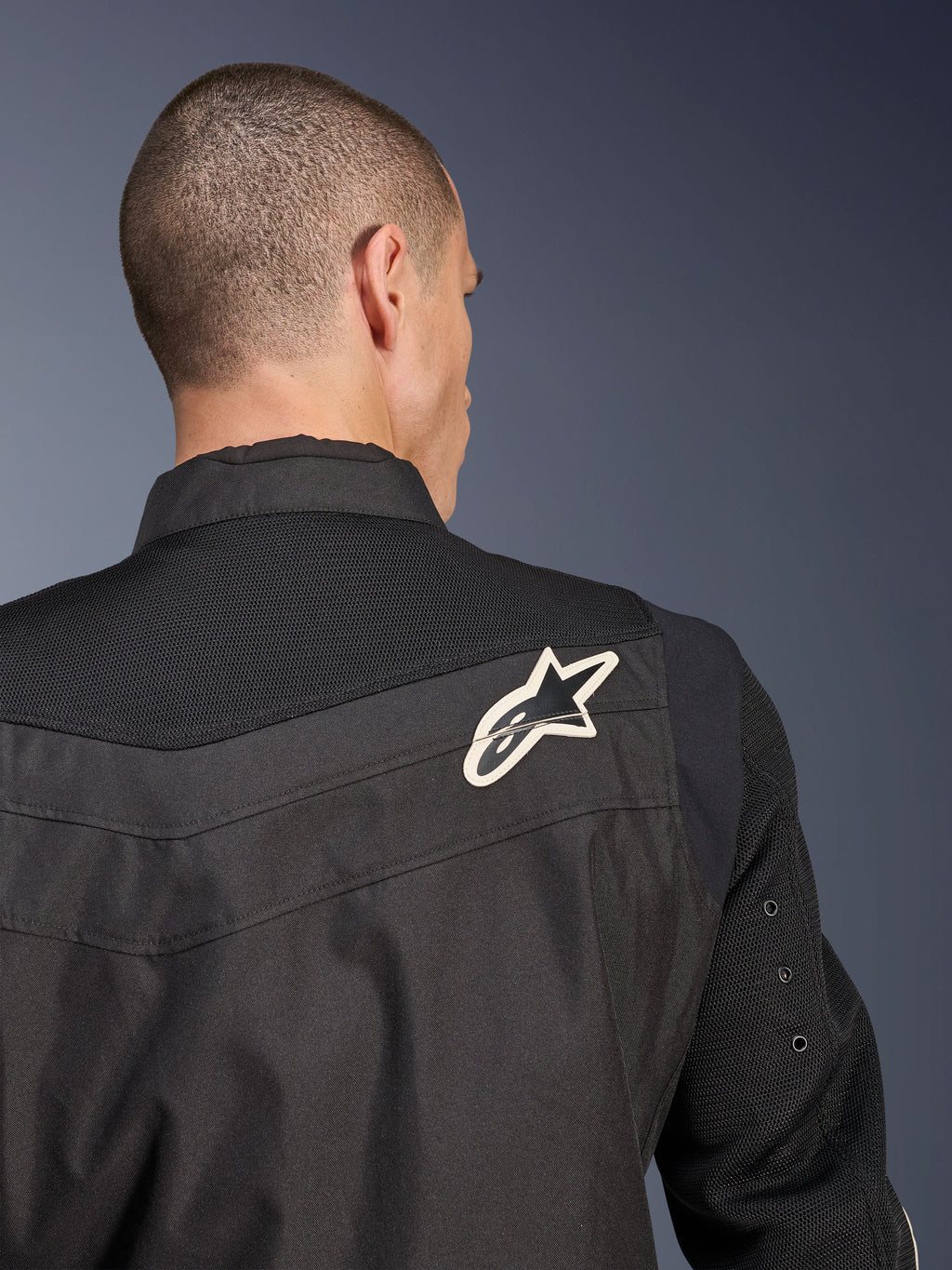 Alpinestars T-Dyno Air Jacket, zwarte textiele motorjas, close-up achteraanzicht met de nadruk op het ademende 3D-mesh op het schouderstuk en de mouwen, voorzien van een wit en zwart sterlogo op de rechterschouder.