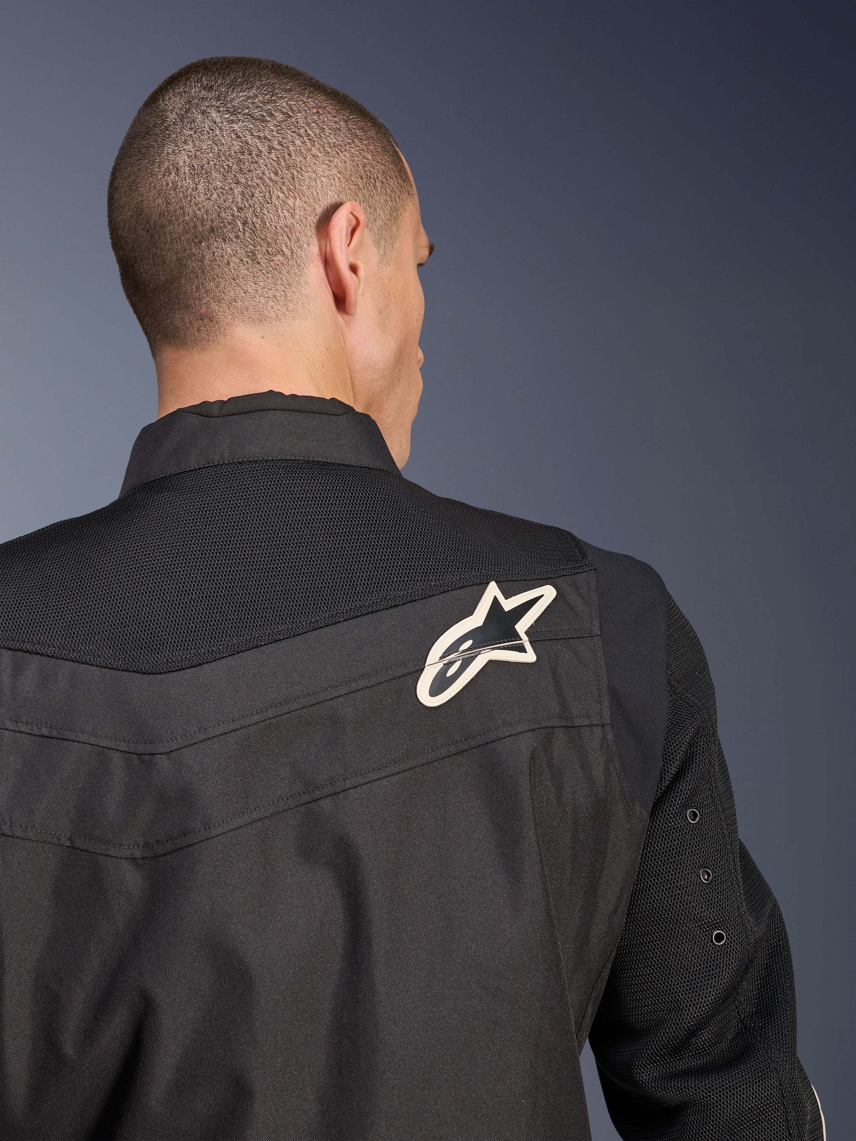 Alpinestars T-Dyno Air Jacket, zwarte textiele motorjas, close-up achteraanzicht met de nadruk op het ademende 3D-mesh op het schouderstuk en de mouwen, voorzien van een wit en zwart sterlogo op de rechterschouder.