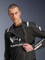 Alpinestars T-Stunt Air Jacket, zwart-witte motorjas, mannelijk model toont een gedeeltelijk opengeritst modulair voorpaneel dat mesh-ventilatielagen onthult, witte Alpinestars-logo's op de borst en mouwen, sportief ontwerp voor rijden op de weg