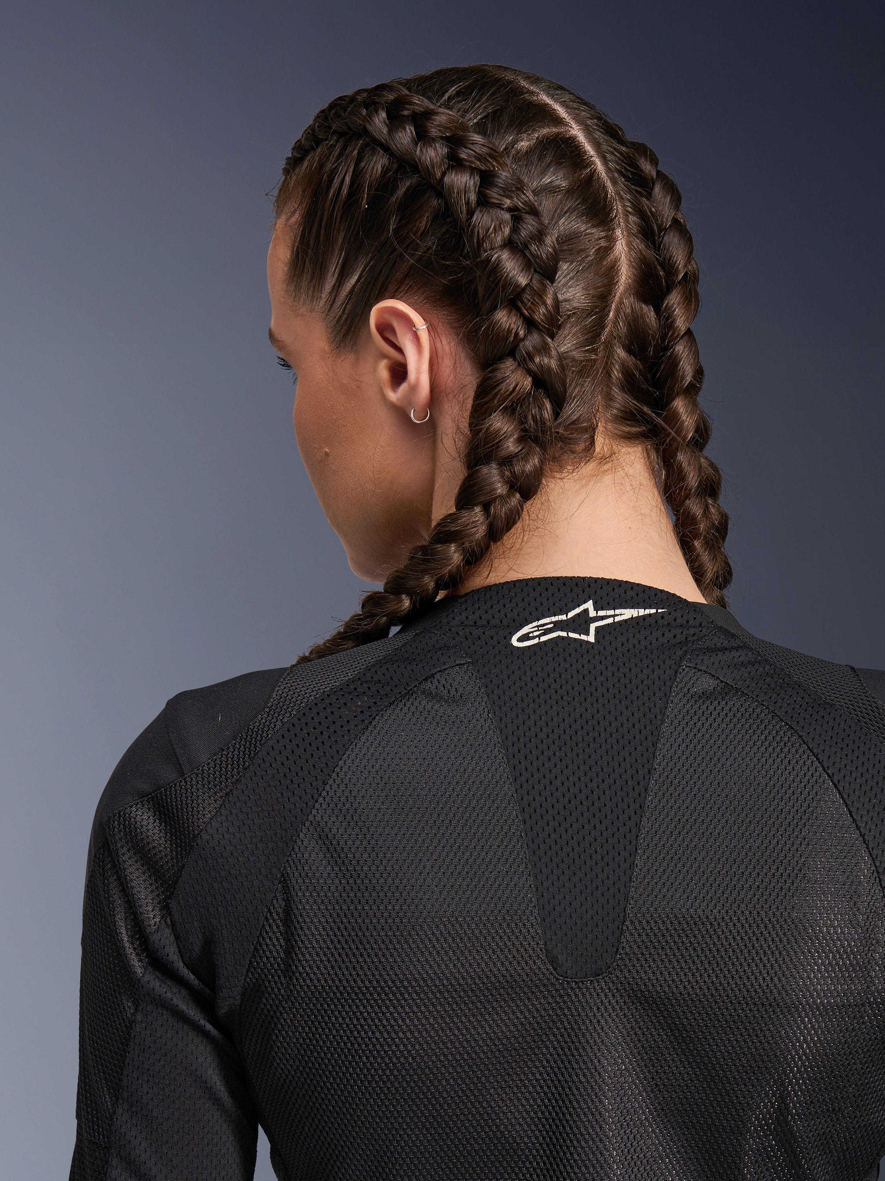Alpinestars Stella Troop-Air damesjas, zwart, gedetailleerd achteraanzicht van de bovenrug en nek, vrouw met ingevlochten haar, voorzien van een wit Astars-logo op de kraag en lichtgewicht 2D tech mesh-stof voor ventilatie