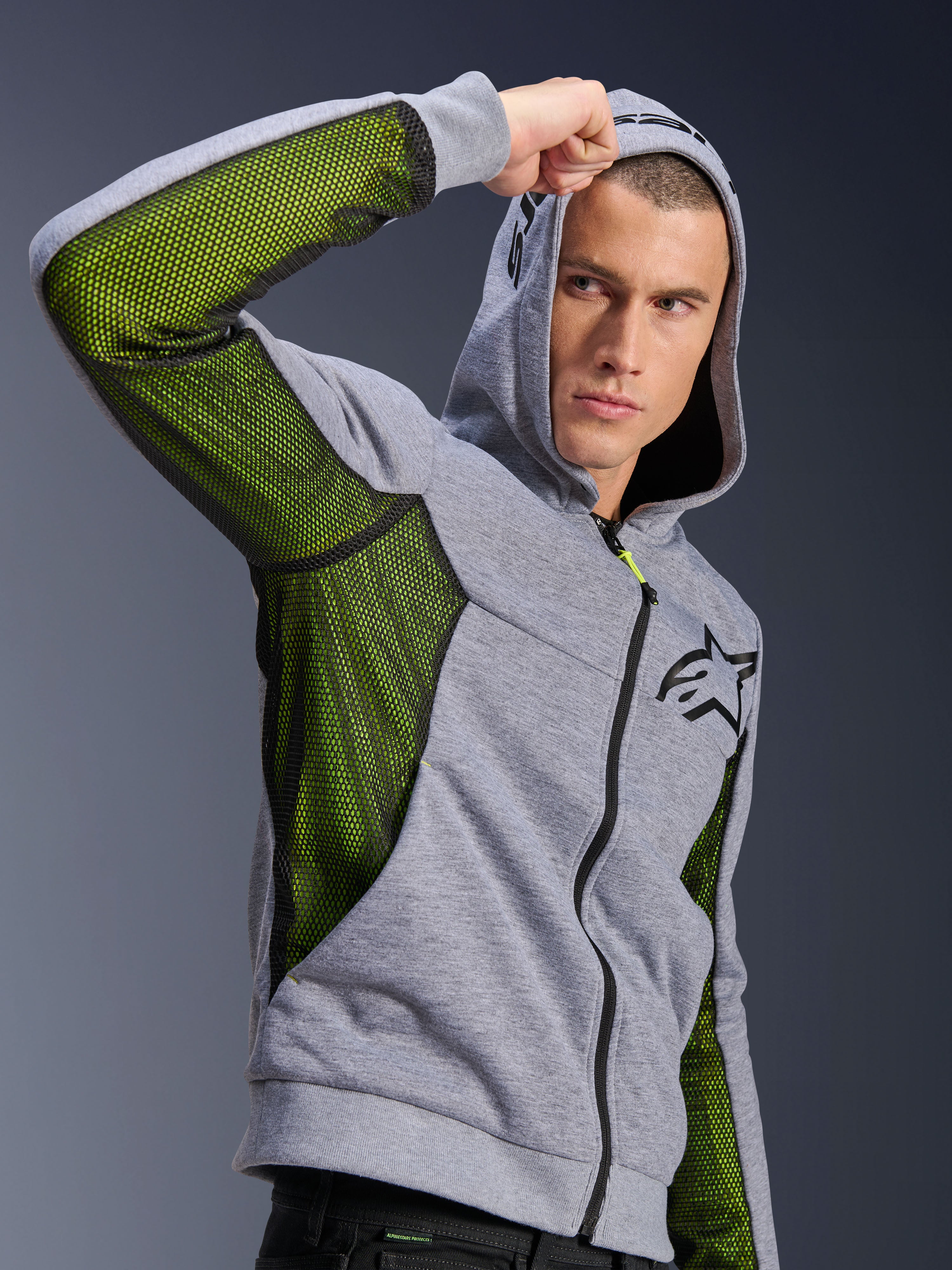 Alpinestars Chrome Air Sport Hoodie, grijs gemêleerd en zwart, voorzien van felgroene mesh ventilatiepanelen aan de zijkant en onder de mouwen, tech fleece materiaal met capuchon, zwart Alpinestars-logo op de borst, stedelijke motorkleding