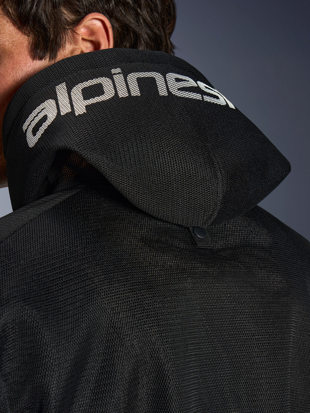Alpinestars Chrome Superairflow Hoodie, zwart, detailweergave van de 3D-mesh capuchon met witte Alpinestars-branding over de bovenkant, inclusief de stabilisatiedrukknoop aan de achterzijde, geventileerde textiele motorkleding voor extreme hitte