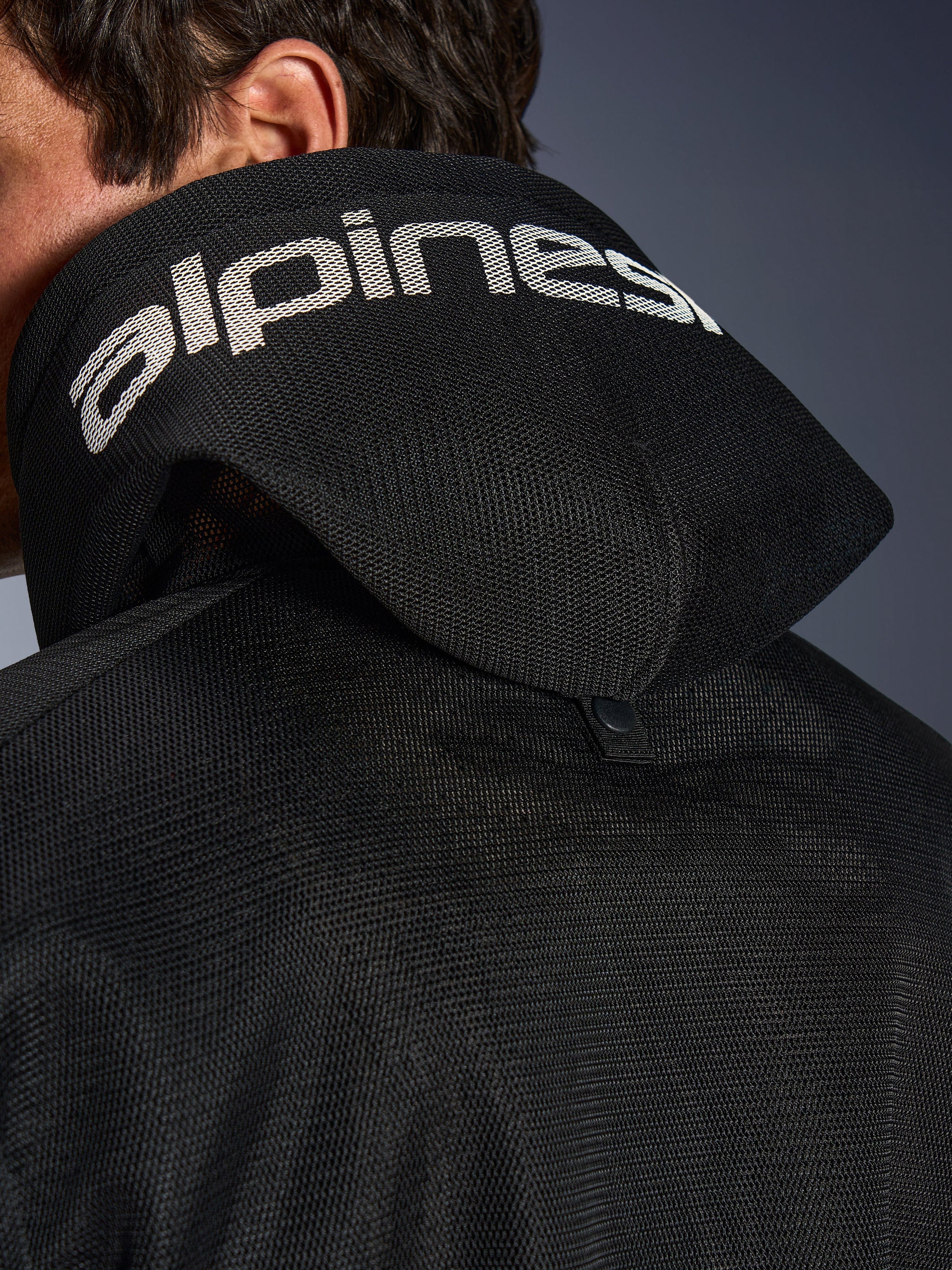 Alpinestars Chrome Superairflow Hoodie, zwart, detailweergave van de 3D-mesh capuchon met witte Alpinestars-branding over de bovenkant, inclusief de stabilisatiedrukknoop aan de achterzijde, geventileerde textiele motorkleding voor extreme hitte